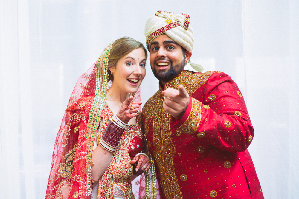 A wedding couple both point towards the camera at the Foundry at Puritan Mill